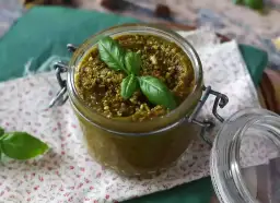 Słoik z pysznym, domowym pesto pistacjowym, ozdobiony listkami bazylii. Idealne do makaronu i kanapek.