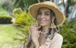 Kasia nastraja pozytywnie w słomkowym kapeluszu i boho biżuterii, uśmiecha się na tle zieleni.
