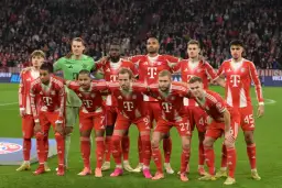 Drużyna Bayern Monachium – zawodnicy w czerwono-białych strojach pozują do zdjęcia na murawie stadionu, z trybunami pełnymi kibiców w tle.
