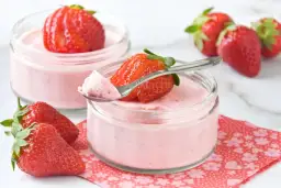 Delicioso mousse de fresa en vasitos, decorado con fresas frescas y una cucharita lista para probar.