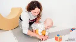 Mama wspiera 2-miesięczne dziecko w pierwszych próbach raczkowania. Zabawy z maluszkiem na macie.