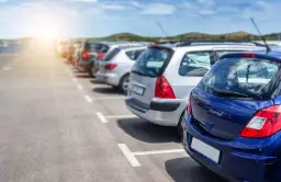 Rząd zaparkowanych samochodów na parkingu, z niebieskim samochodem na pierwszym planie.