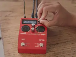 Dłoń kręci gałką na czerwonym looperze do gitary Boss RC-10R, ustawiając rytm funk.