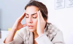 Femme se tenant les tempes, l'air soucieux. Comment toucher 100 % de son salaire en arrêt maladie ?