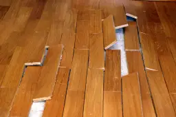 Parquet en bois abîmé, lames décollées et cassées. Une vraie malfaçon de travaux qui rend le sol dangereux.