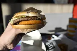 Dłoń trzyma burgera McDouble z podwójnym kotletem i chrupiącą warstwą.
