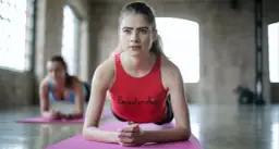 Kobiety wykonujące ćwiczenie plank na macie w sali gimnastycznej.