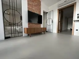 Nowoczesne wnętrze z betonową podłogą, co to jest mikrocement, która nadaje mu surowego charakteru. W tle widać łazienkę i salon.