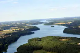 Malowniczy widok na jezioro Raduńskie Dolne otoczone lasami i polami. W oddali widać zabudowania.