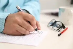 Dłoń pisze na formularzu, obok okulary i kubek. Zastanawiasz się, na co zwrócić uwagę przy kredycie hipotecznym?