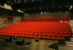 Widok na puste czerwone fotele w sali kinowej lub teatralnej.