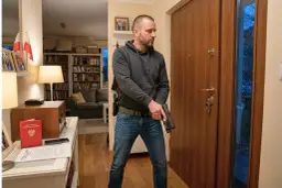 Mężczyzna z pistoletem przy drzwiach, gotowy do obrony przed naruszeniem miru domowego. Na stole legitymacja posiadacza broni.