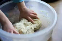 Dziecko zagniata ciasto w misce. Czy weganie jedzą drożdże? Tak, drożdże to grzyby, więc są wegańskie.