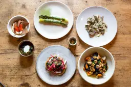 Assortiment de plats gastronomiques : asperges, moules, tartare, et autres mets fins sur table en bois.