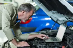 Mechanik z laptopem przy silniku samochodu.