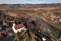 Widok z lotu ptaka na malowniczą dolinę Popradu zimową porą. Biały kościół z czerwoną wieżą góruje nad zabudowaniami.