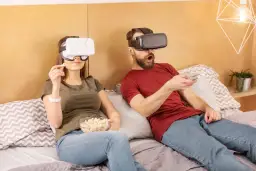 Para ogląda filmy VR na kanapie, trzymając popcorn i pilota.
