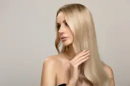 Kobieta z pięknymi, długimi włosami w odcieniu brzoskwiniowy blond, delikatnie dotyka ich dłonią.