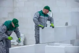 Pracownicy budowlani kontynuują murowanie ścian z bloczków, mimo ryzyka nocnych przymrozków. Szybkie tempo prac jest kluczowe.