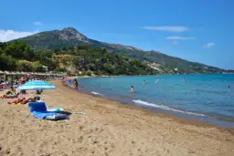 Słoneczna plaża na Zakynthos w czerwcu. Ludzie kąpią się w turkusowym morzu, opalają pod parasolami. Idealna pogoda na wakacje.
