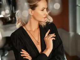 Elegancka kobieta w czarnej sukience z głębokim dekoltem i złotą biżuterią.