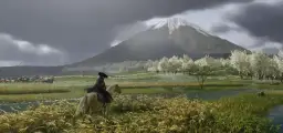 Jazda konna w Ghost of Tsushima PC. W oddali widać ośnieżony szczyt góry, a na pierwszym planie kwitnące drzewa i rzekę.