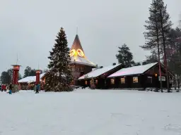 Śnieżny krajobraz z choinką i budynkami, gdzie znajduje się dom Świętego Mikołaja.