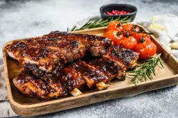 Soczyste żeberka w sosie BBQ, podane z pieczonymi pomidorkami i rozmarynem. Idealne na obiad lub grilla.