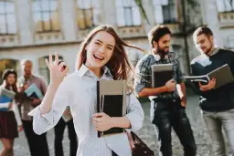 Uśmiechnięta studentka z notatnikami pokazuje znak OK. Pokazuje, jakie są perspektywy dla osób z wykształceniem humanistycznym – świetlane!
