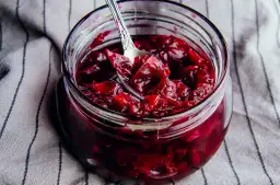 Słoik pełen aromatycznej konfitury z płatków róży, z łyżeczką zanurzoną w rubinowym, gęstym dżemie.