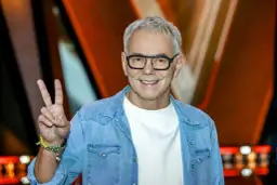 Robert Janowski, syn księdza, w dżinsowej koszuli i okularach, pokazuje znak pokoju.