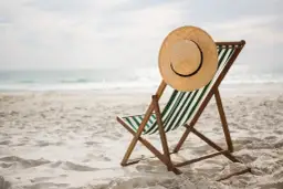 Leżak plażowy z kapeluszem na oparciu, gotowy na wczasy pod gruszą. Piasek, morze i słońce czekają.