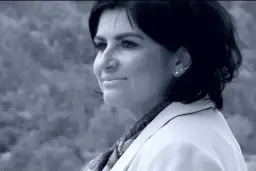 Portret Agnieszki Kołacz Leszczyńskiej w białej marynarce, z delikatnym uśmiechem i ozdobnymi kolczykami.