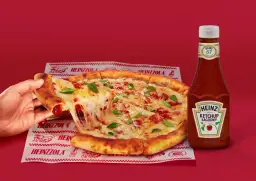 Ciepła pizza z ciągnącym serem i bazylią, obok butelka łagodnego ketchupu Heinz – idealny duet do każdego kęsa.