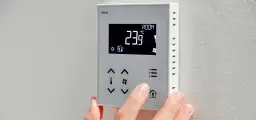 Dłoń reguluje termostat, pokazując jak ustawić temperaturę na pompie ciepła. Aktualna temperatura to 23.9°C.