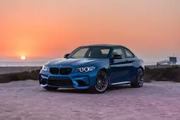 Niebieskie BMW M2 z pakietem M na plaży o zachodzie słońca. To jest m pakiet, który nadaje autu sportowy wygląd i osiągi.