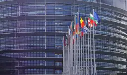 Flaga Unii Europejskiej i flagi państw członkowskich przed nowoczesnym budynkiem.