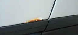 Małe ogniska rdzy na białym samochodzie, tuż nad czarną listwą. Czas na ich usunięcie!
