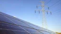 Panele fotowoltaiczne i linia energetyczna pod błękitnym niebem. Zastanawiasz się, jak zresetować fotowoltaikę?
