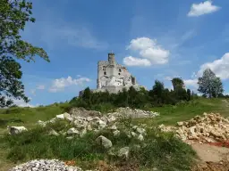 Ruiny zamku Bobolice na wzgórzu, otoczone zielenią i kamieniami.
