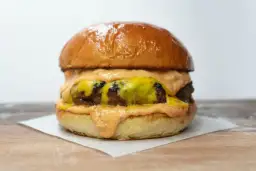 Soczysty burger z roztopionym serem i sosem na jasnym tle.
