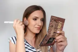 Kobieta nakłada puder pędzlem, trzymając w dłoni paletkę do konturowania. Efekt subtelnego makijażu no makeup.