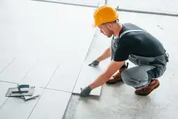 Fachowiec w żółtym kasku układa płytki. Zastanawiasz się, ile kosztuje położenie płytek za metr?