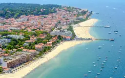 Vue aérienne d'une ville côtière avec une plage bondée et des bateaux dans l'eau.