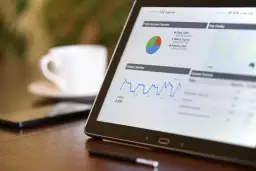 Tablet z wykresami ruchu na stronie, pokazujący dane do promowania strony w Google. Obok filiżanka kawy.