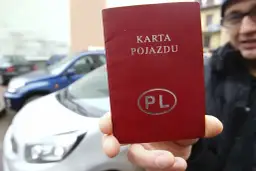 Czerwona karta pojazdu z napisem "KARTA POJAZDU" i symbolem "PL" w owalu, trzymana przed białym samochodem.