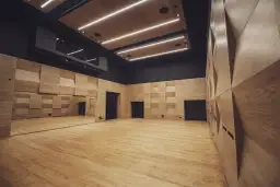 Nowoczesna sala prób w Teatrze Ludowym w Krakowie. Drewniane ściany i podłoga, lustra i oświetlenie tworzą inspirującą przestrzeń.