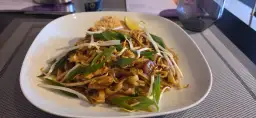 Pad thai z kurczakiem, kiełkami fasoli mung, szczypiorkiem i ćwiartką limonki na białym talerzu.