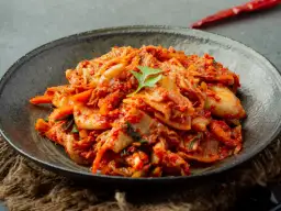 Miseczka z pikantnym kimchi, ozdobiona listkiem kolendry.