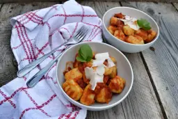Dwa talerze pysznych gnocchi z sosem pomidorowym, posypane parmezanem i udekorowane bazylią, gotowe do podania.
